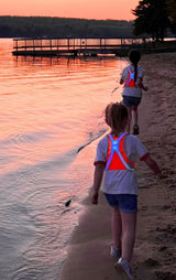 Rennende kinderen langs het water met een NoxGear Tracer Junior verlicht harnas om.